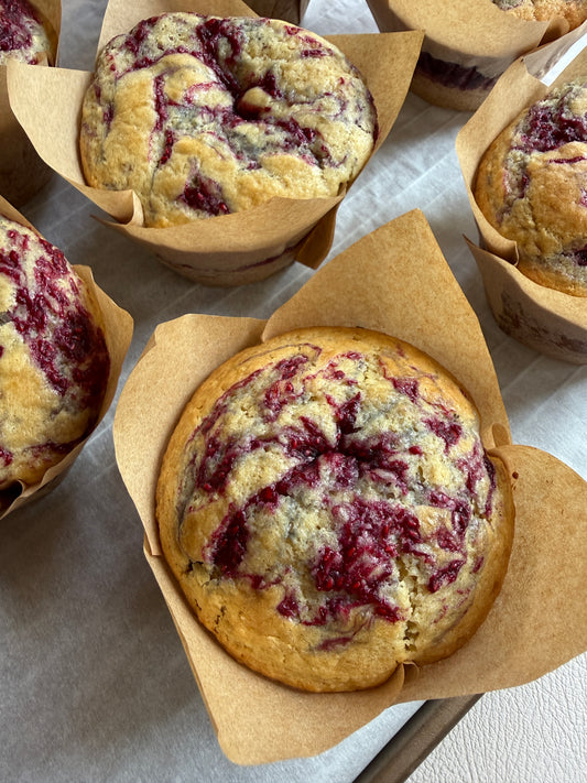 Muffins with raspberry swirl in brown paper cups on a light surface